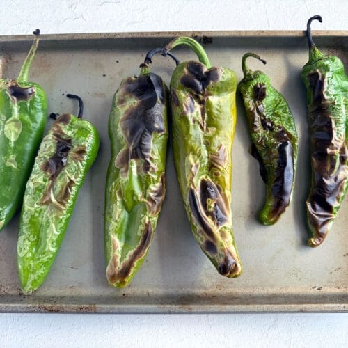 Six roasted green chiles on a baking sheet.