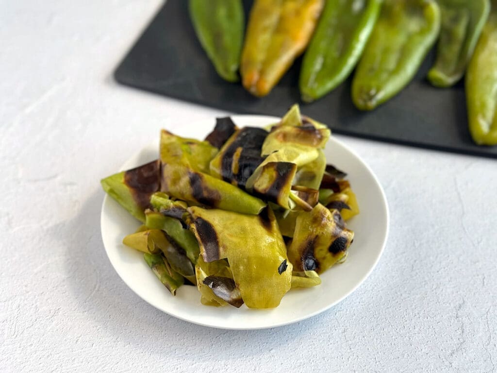 Blistered skins of peppers on a white plate.