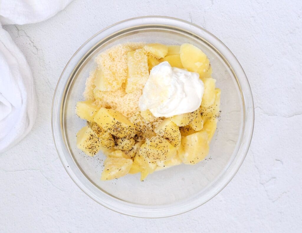 Cubed potatoes and sour cream in a clear glass bowl.