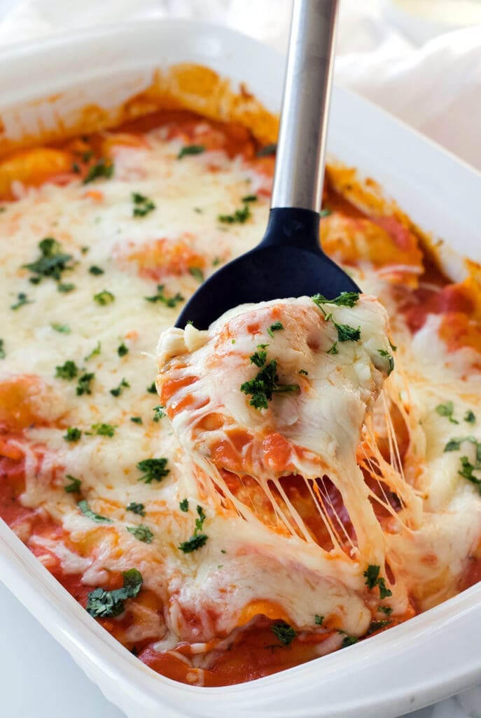 A black spoon serving freshly baked ravioli casserole.