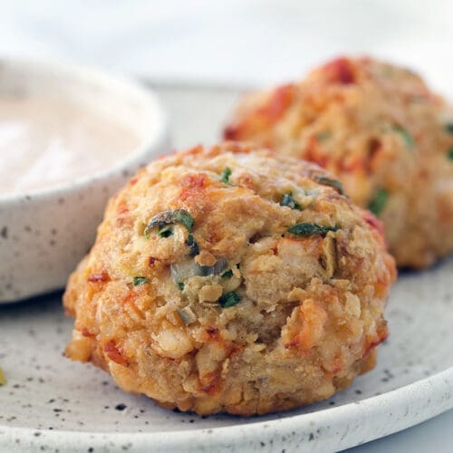 Two lobster cakes on a plate with lemon slices.