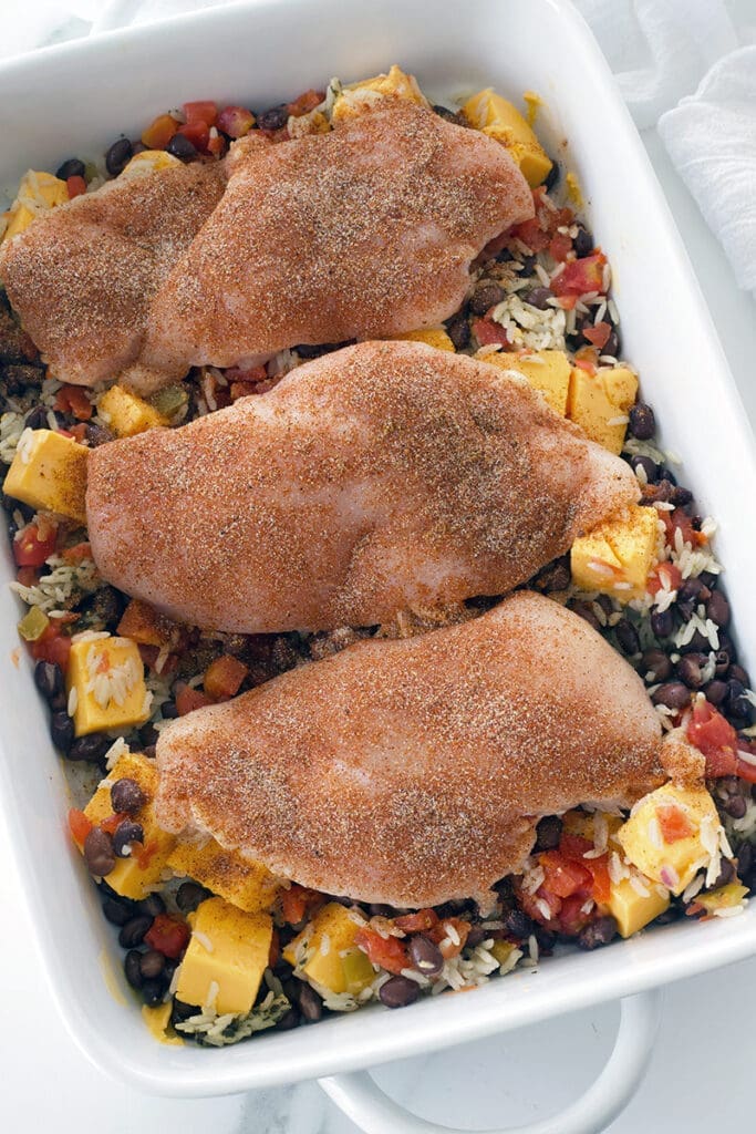 Raw chicken with beans and rice on a baking plate.
