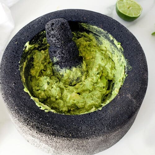 Morcajete guacamole next to coriander and lime.