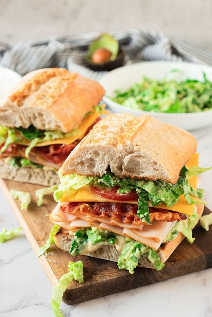 The Turkish and avocado sandwich was cut into half of a cutting board.