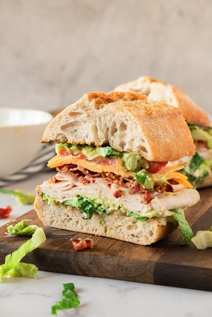 Half of a turkey avocado with a bacon sandwich on a cutting board.
