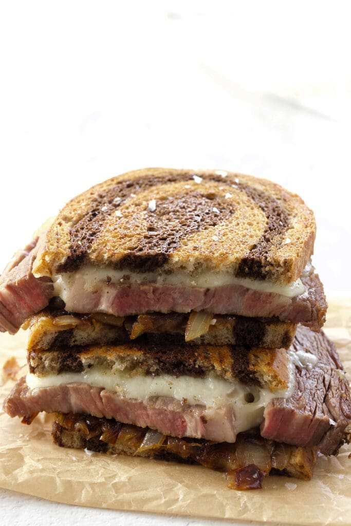 Prime rib patty melt cut in half on parchment paper.