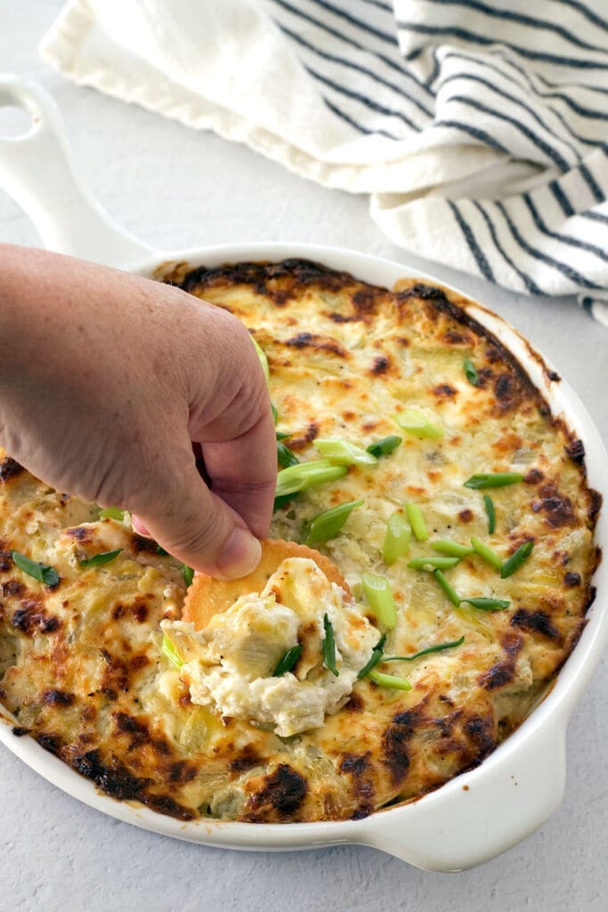 Hand with a ritz scooping a baked appetizer in a white dish.