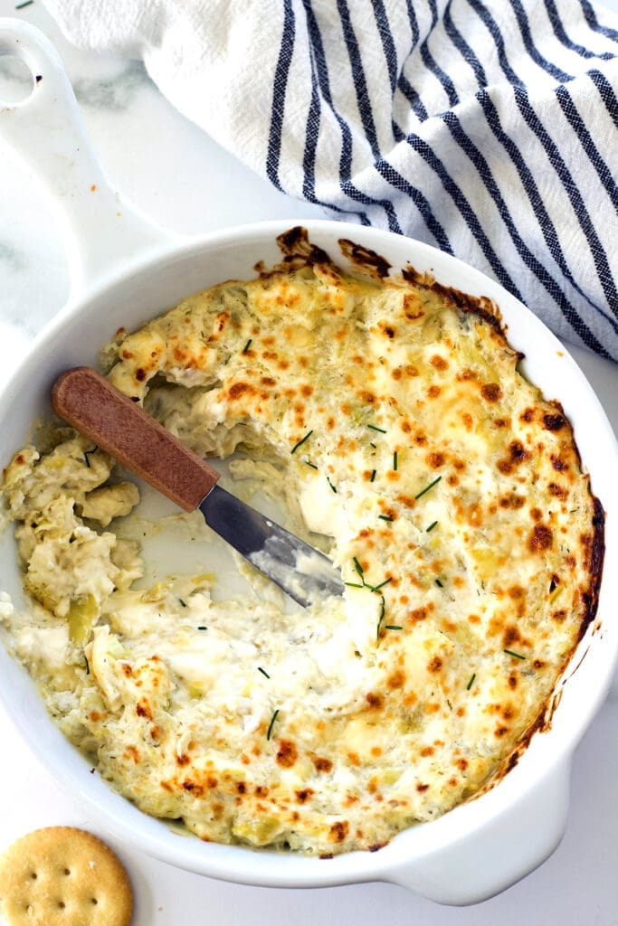 Baking dish with a knife resting on the hot artichoke dip inside.
