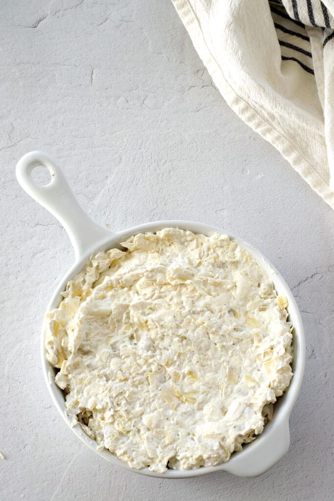 Uncooked crab and artichoke dip in a baking dish.