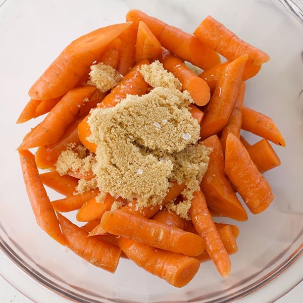 Raw carrots and sugar in a clear bowl.