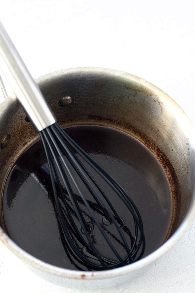 Silver pan with a whisk and dark liquid inside.