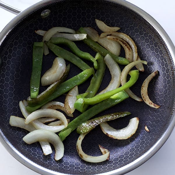 Peppers and onions for Philly cheesesteak in a black skillet.