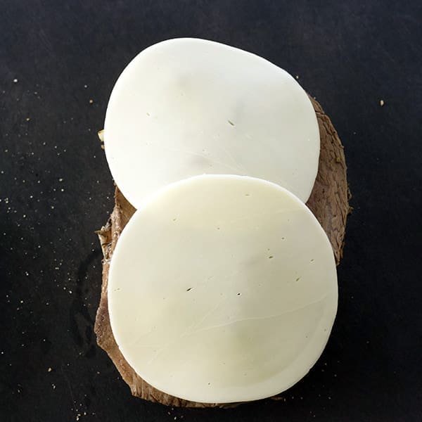 Two round pieces of cheese on a black cutting board.