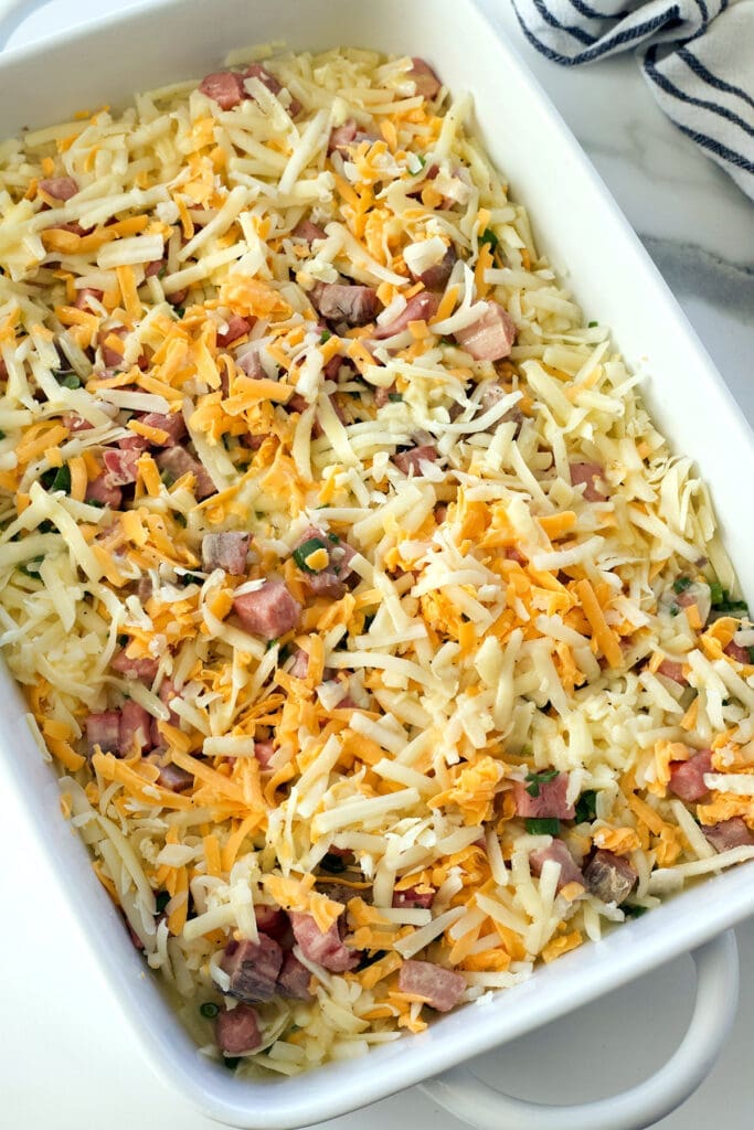uncooked cheese, eggs and meat in a white baking dish.