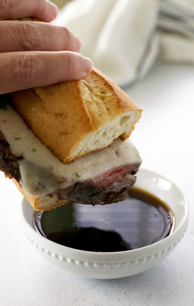 Hand holding a roast beef sandwich dipping in au jus