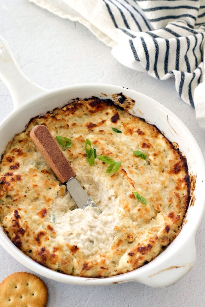 A white bowl of crab dip with a knife in the middle.