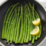 Saut&eacute;ed Asparagus and lemon wedges in a black skillet.
