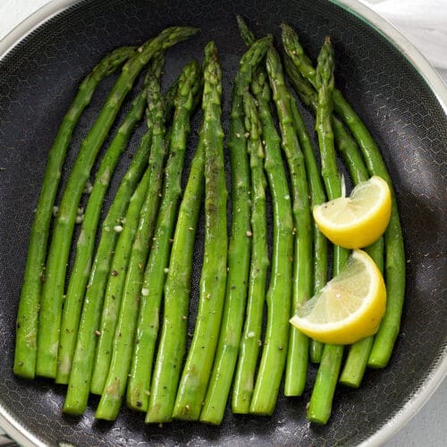 Saut&eacute;ed Asparagus and lemon wedges in a black skillet.