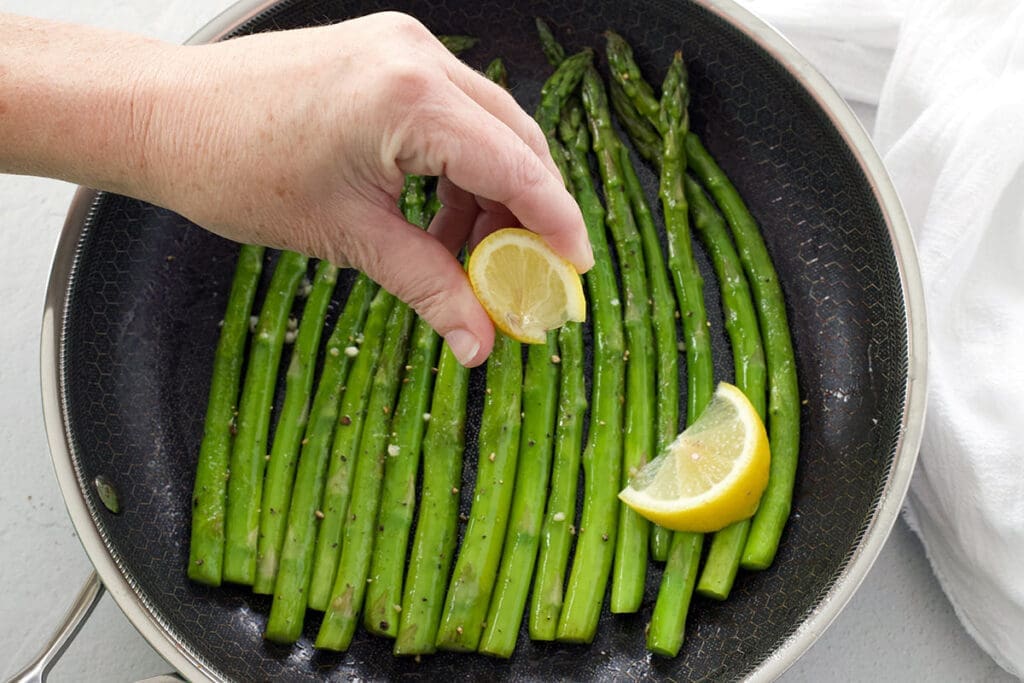 Hand squeezing lemon over cooked green vegetables.