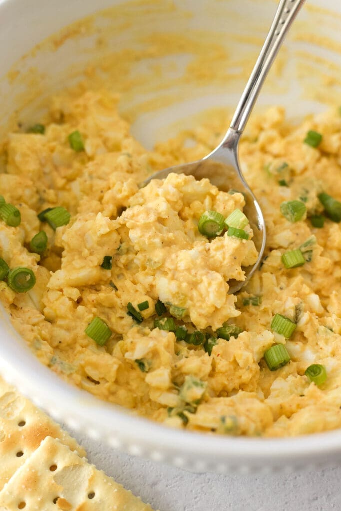 Spoon scooping up salad in a white bowl.