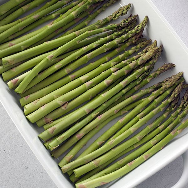 Uncooked asparagus in a white baking pan.