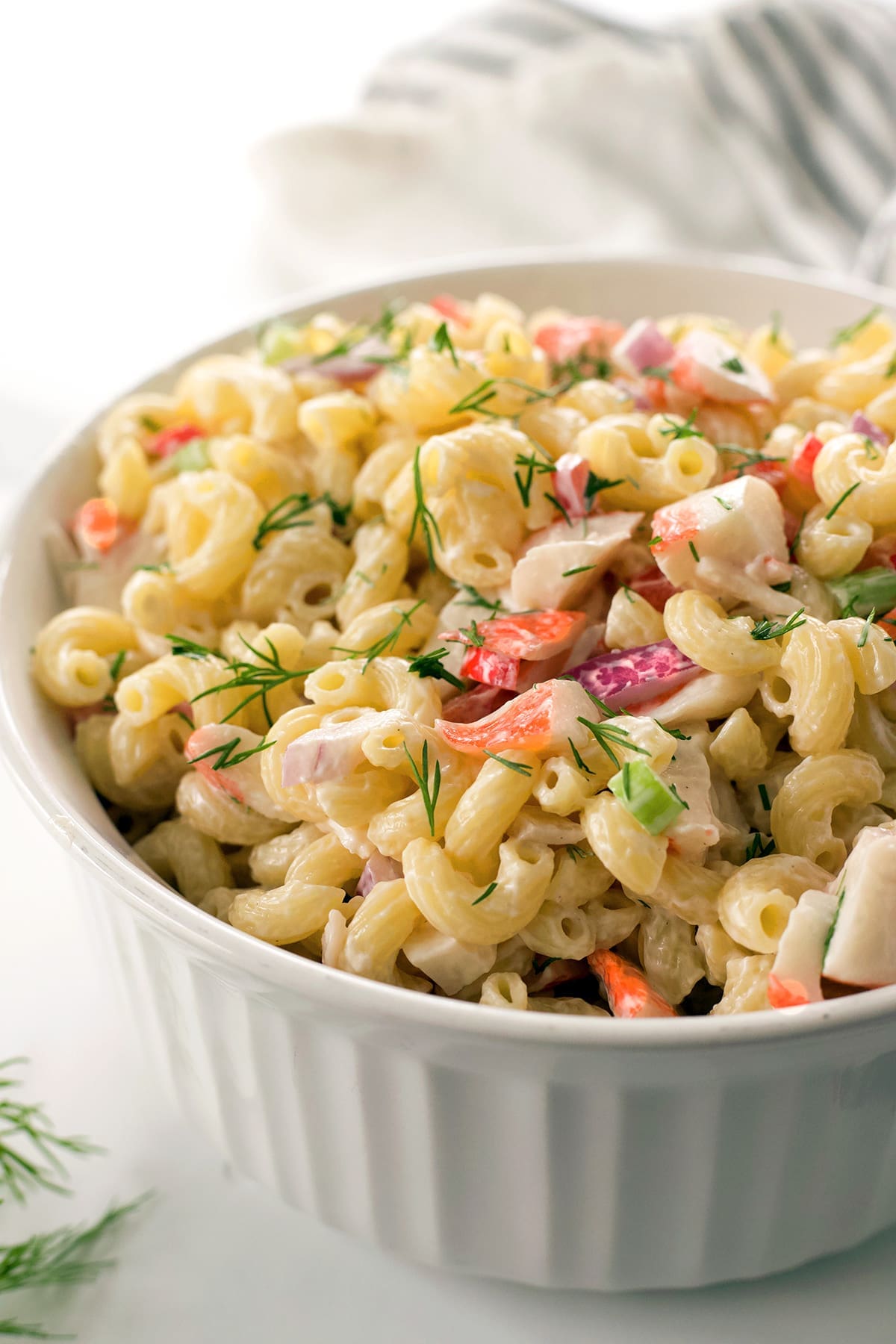 A generous white bowl of crab pasta salad with fresh dill.