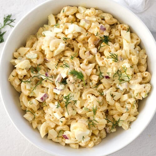 Deviled egg pasta salad in a white bowl next to fresh dill.