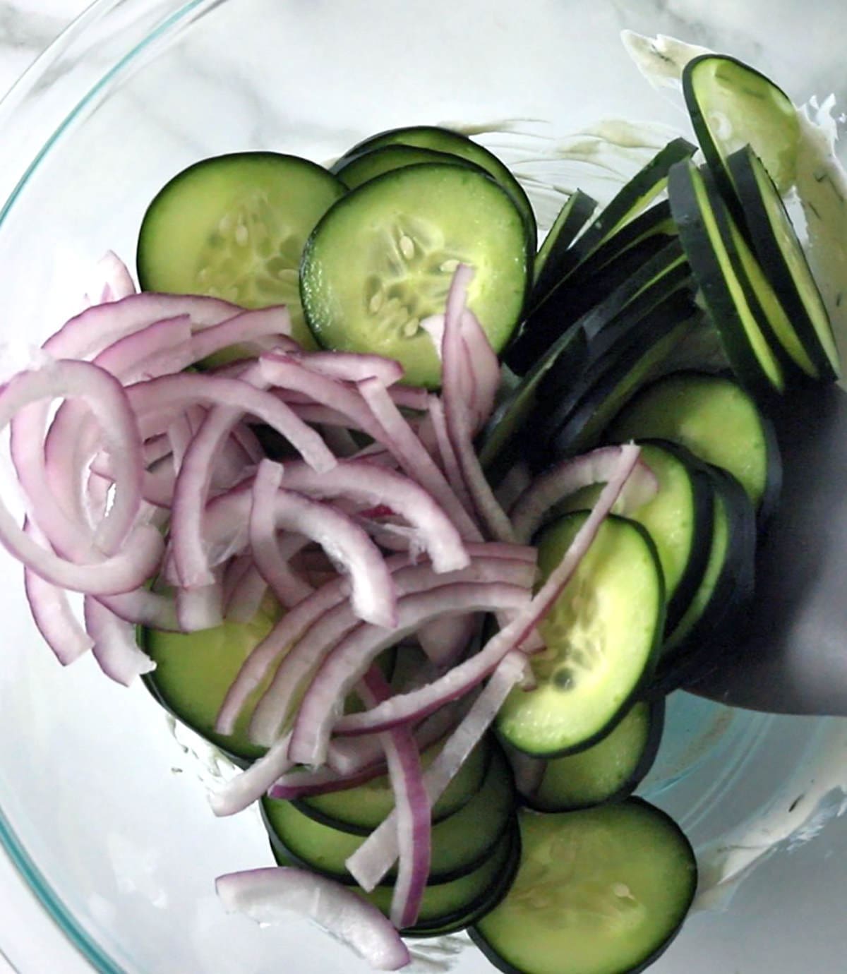 Glass bowl with cut cucumbers and onions.