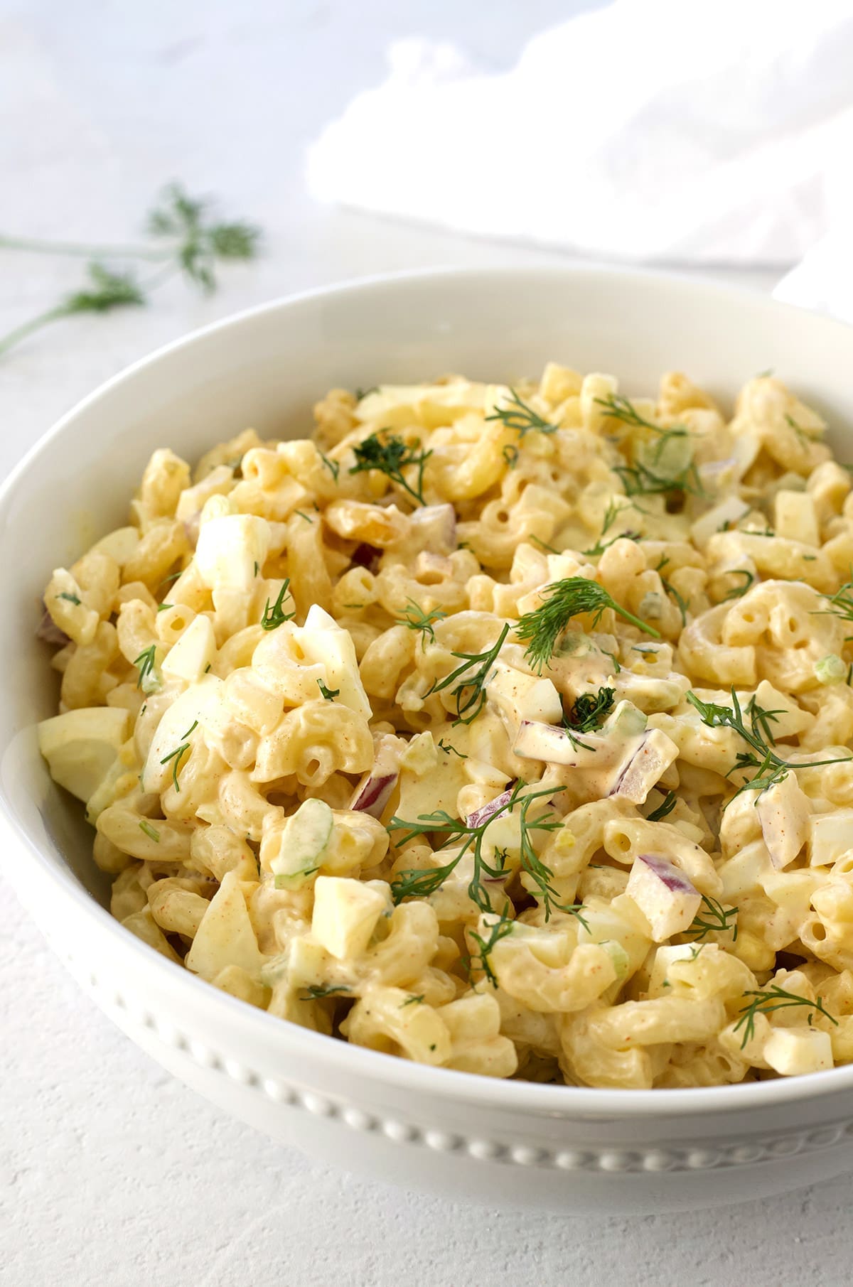 White bowl with creamy macaroni mix and fresh dill.