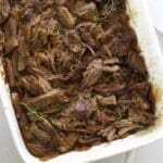 Chuck roast in the oven shredded in a white baking dish.