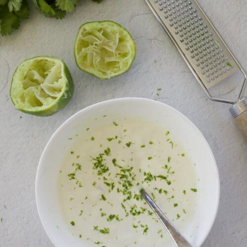 Small bowl of cilantro lime crema with a grater and juiced lime.
