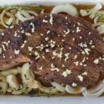 Chuck roast in a white pan surrounded by sliced onions for how to cook chuck roast article.