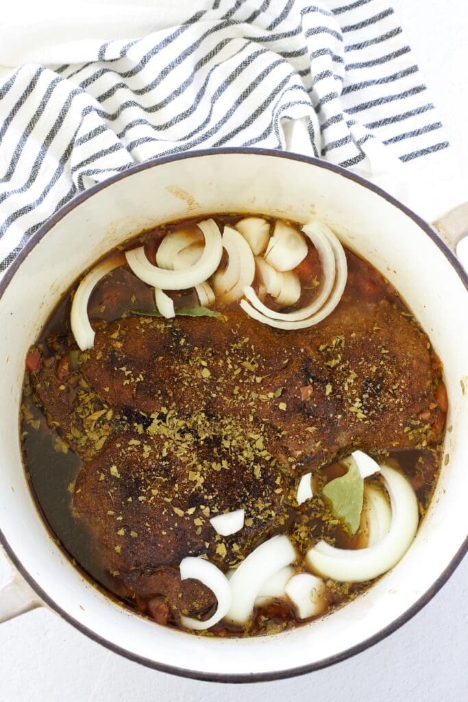 Chuck roast, onions, and brown liquid in a dutch oven.