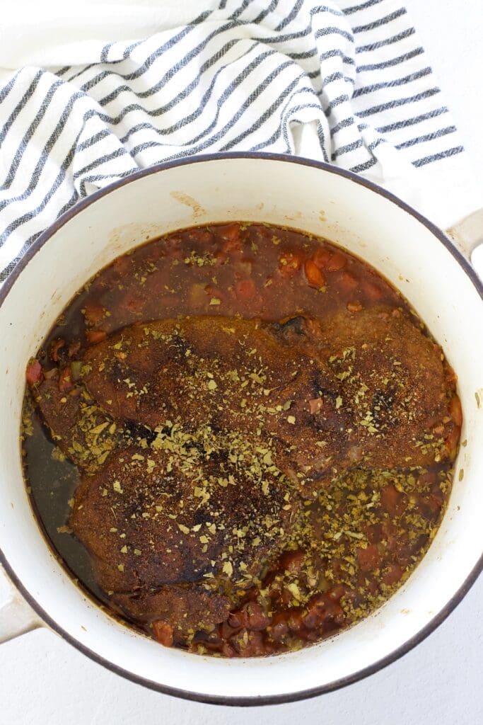 Cooked beef in braising liquid in a cream dutch oven.