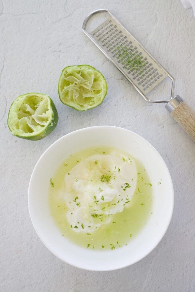 Bowl of lime juice and sour cream next to squeezed limes.