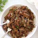White bowl full of Mexican shredded beef and two forks.
