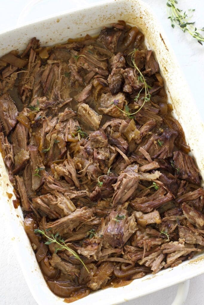 Shredded chuck roast in a white baking pan to make french dip sandwiches.