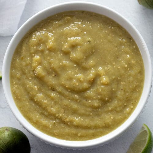 Salsa Verde in a white bowl with tomatillos and lime.