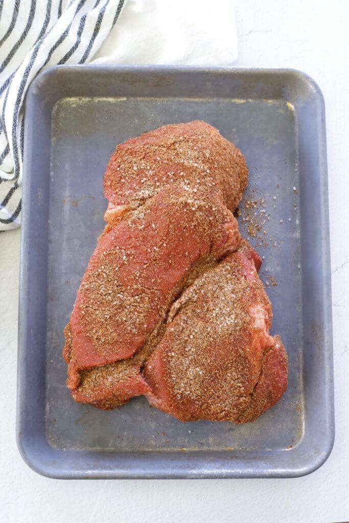 Seasoned raw chuck roast on a metal baking sheet.