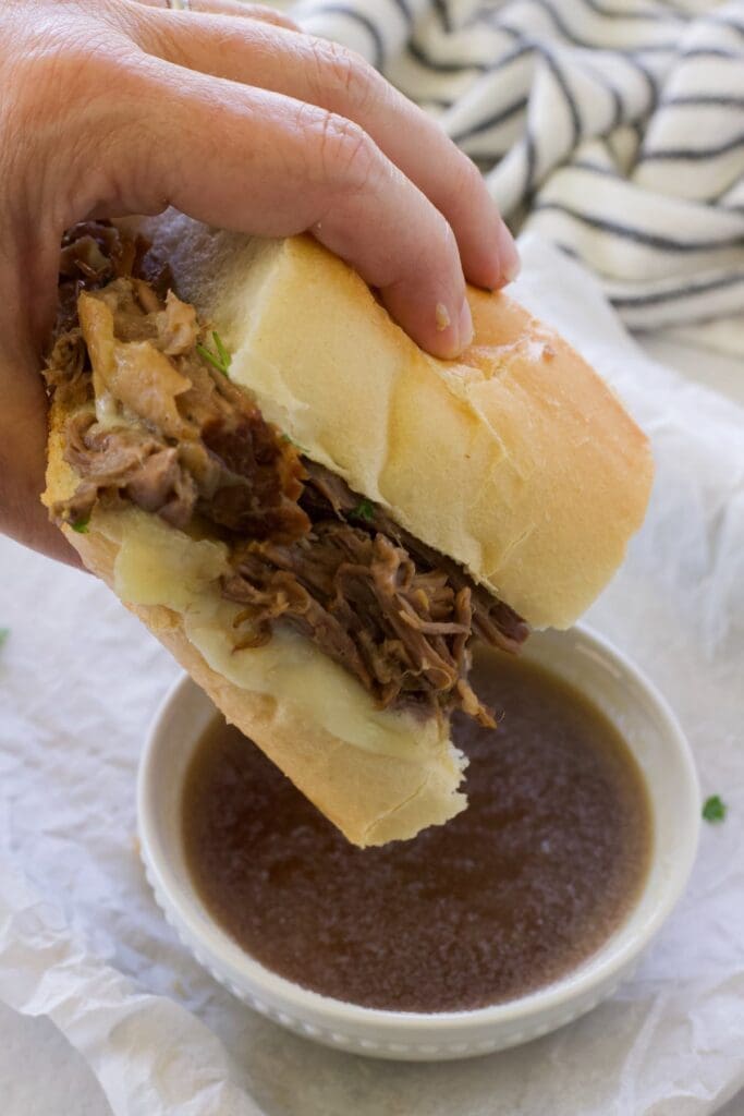 hand holding half a sandwich and dipping it in au jus.