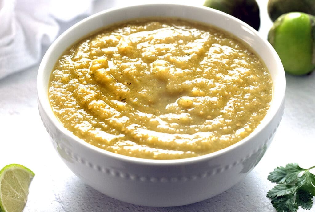 Salsa Verde in a white bowl with tomatillos and lime.