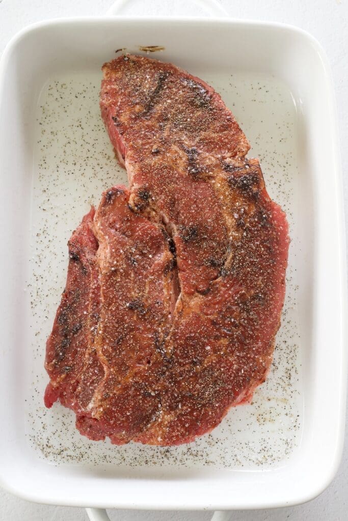 Raw chuck roast coated in bouillon in a baking pan.