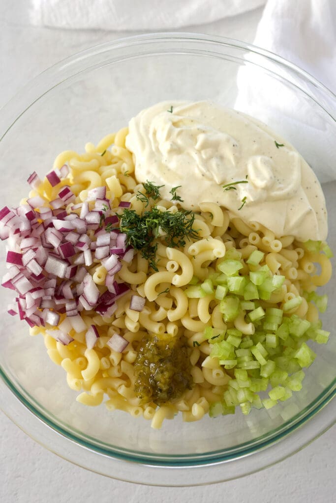 Clear bowl with pasta, onions, relish, celery and dressing.