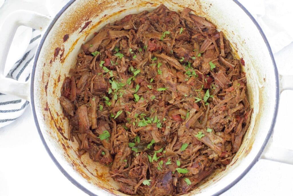 Cream dutch oven full of Mexican shredded beef.