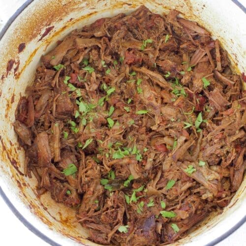Cream dutch oven full of Mexican shredded beef.