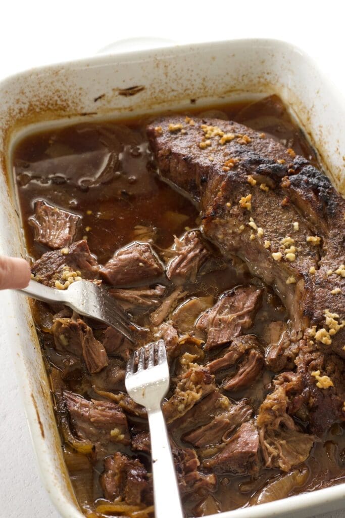 Two forks shredding chuck roast in the oven.