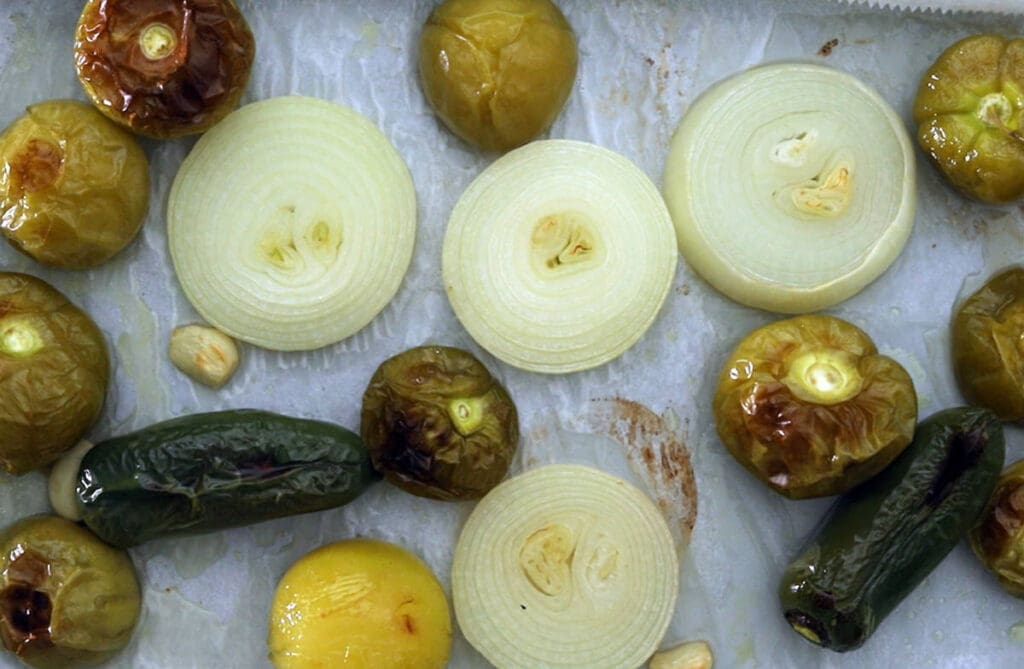 Roasted tomatillos, peppers, and onions on a baking sheet.