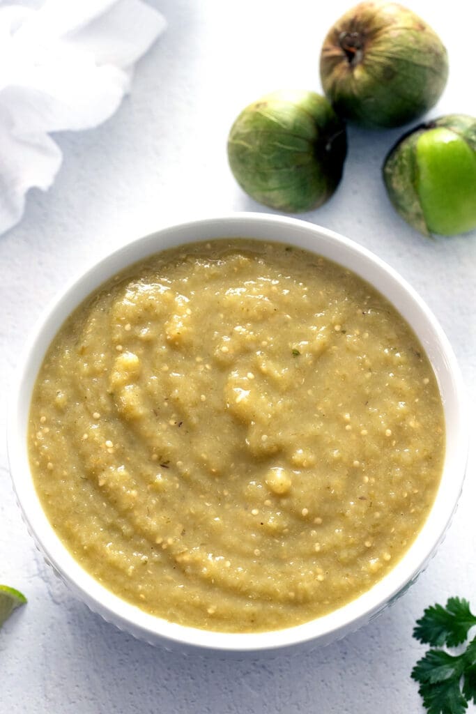 Salsa Verde in a white bowl with tomatillos and lime.