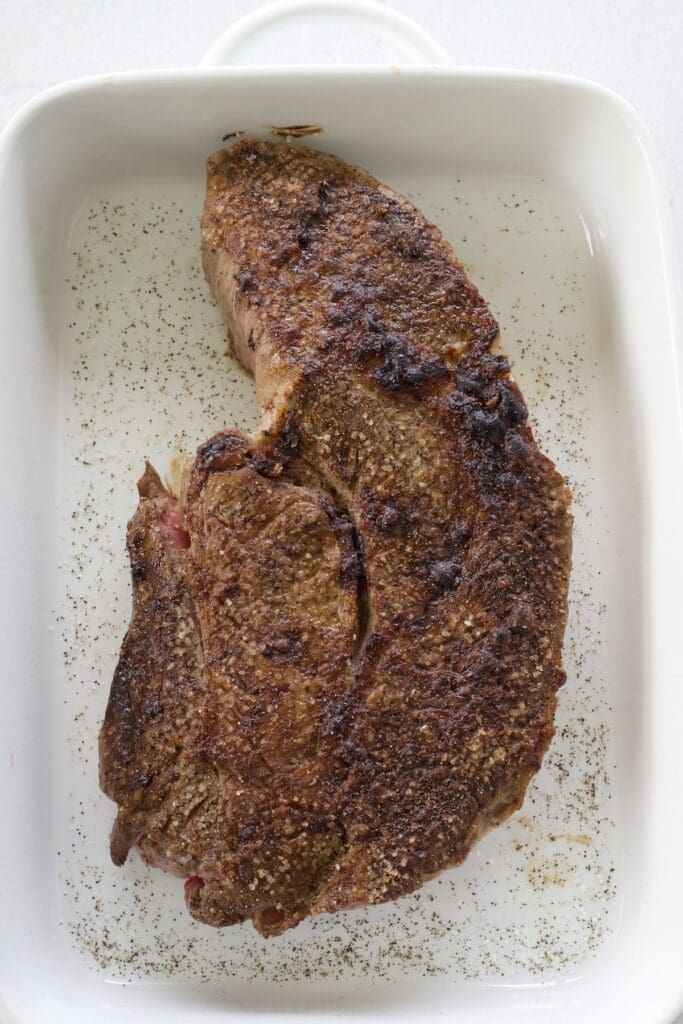 Seared beef in a white baking pan.