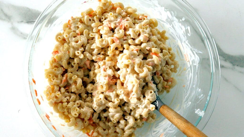 Wooden spoon stirring macaroni salad.